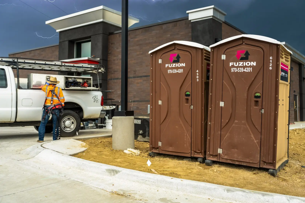 Fuzion portable toilets with construction equipment in the background.